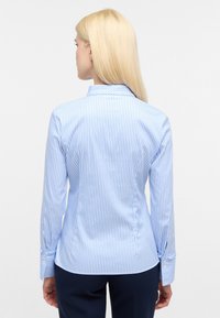 Light blue and white striped button-up shirt, featuring a collared neckline and long sleeves with button cuffs. Smooth fabric texture.