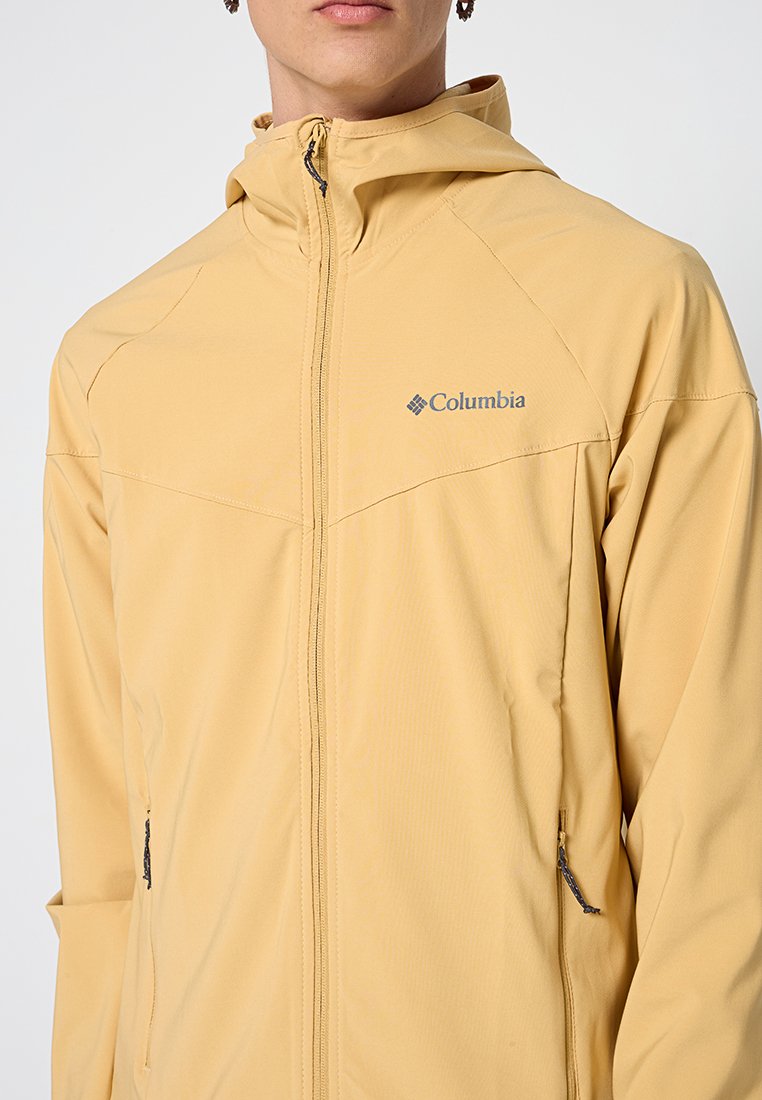 Żółta lekka kurtka z kapturem, z zamkiem błyskawicznym i dwiema bocznymi kieszeniami. Z przodu na piersi znajduje się szare logo Columbia. Gładka tekstura.