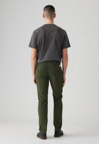 Camiseta gris oscuro y pantalones de pana verde olivo vistos desde atrás. Los pantalones cuentan con bolsillos laterales y traseros, combinados con zapatos negros.