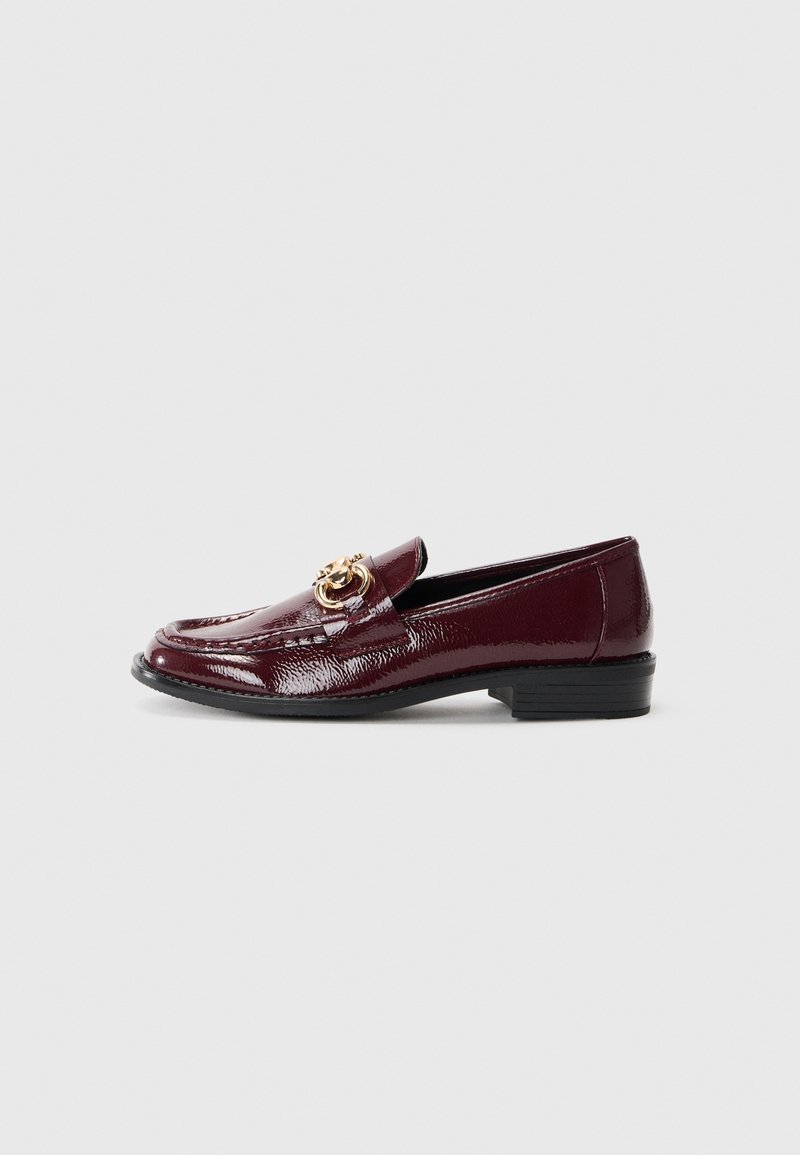 Mocassin en cuir verni bordeaux avec un petit talon noir, décoré d'un accessoire en métal doré sur le devant. Texture lisse.