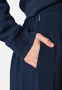 Marineblaues Sweatshirt mit gerippten Bündchen und seitlicher Tasche. Der Stoff scheint weich mit einer glatten Textur und leichtem Glanz zu sein.