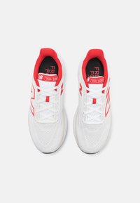Ténis atléticos brancos com detalhes em vermelho, parte superior em malha, atacadores planos e sola de borracha. Apresenta as marcas "Fresh Foam" e "1080" na língua.