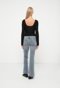 Un haut à manches longues noir avec un dos en scoop, associé à un jean fluide bleu clair. Le tissu semble doux avec une texture subtile. Des chaussures noires complètent la tenue.