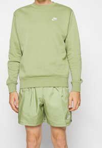 Grön bomullströja med rund halsringning och vit Nike-logotyp, kombinerad med ljusgröna shorts i mjukt, glänsande tyg.