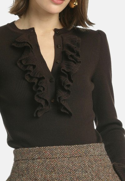 Brązowy sweter prążkowany z głębokim dekoltem w kształcie litery V i falbanami, z guzikami na przodzie, zestawiony z spódnicą w wzór houndstooth.