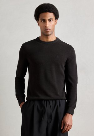 Pull en tricot noir avec col rond et manches longues, présentant une texture subtile. Associé à un pantalon noir ample.