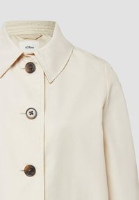 Manteau crème boutonné avec col pointu et quatre boutons foncés, avec étiquette de marque s.Oliver à l'intérieur du col.