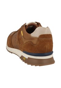 Zapatilla de ante marrón con una tapa de talón de cuero suave, entresuela color crema y un acento amarillo cerca del talón. Diseño texturizado, de estilo atlético con una suela resistente.