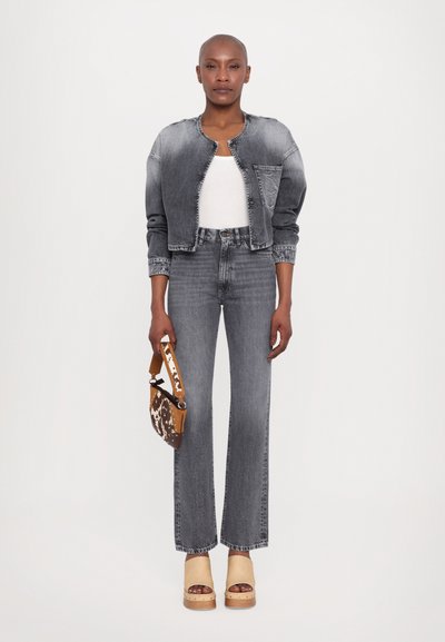 Jachetă din denim gri cu guler rotund, top alb fără mâneci, blugi gri cu croială largă și sandale platformă bej, ținând o geantă de mână cu model maroniu.