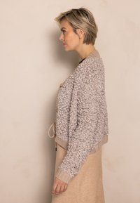 Hellgraue, strukturierte Strickjacke mit pelziger Oberfläche, gerippten Bündchen und verstellbarem Kordelzug am Saum, kombiniert mit einem beigen Rock.