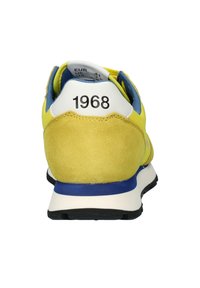 Scarpa sportiva gialla e blu con tomaia in suede, controsole bianco, suola in gomma e il numero "1968" sul tallone.