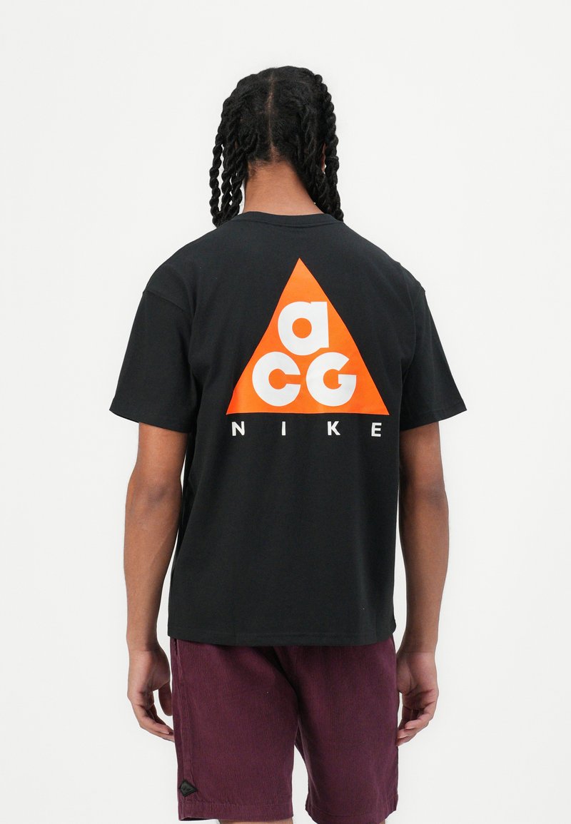 Sort bomulds t-shirt med et stort orange trekantet logo og hvid tekst "acg" samt "NIKE" på ryggen. Korte ærmer og afslappet pasform.