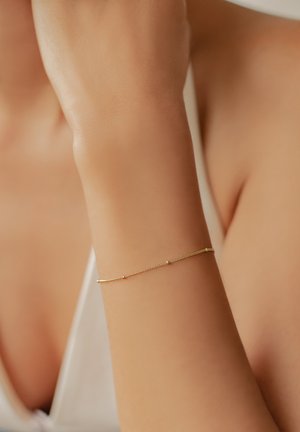 Pulsera de oro con un diseño de cadena delicada, que presenta pequeños acentos coloridos y una textura suave, llevada en una muñeca.