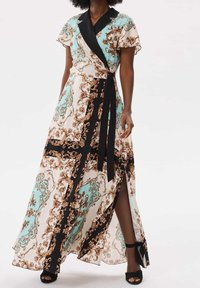 Robe maxi avec une base crème clair ornée d'un motif turquoise et marron, des bordures noires et un design enveloppant avec une fente haute jusqu'à la cuisse.
