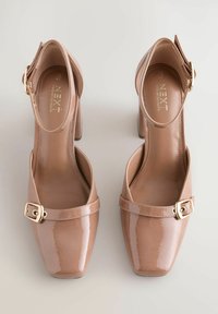 Nude patent leather high heels with a square toe, ankle strap, and gold buckle accent. Smooth texture, block heel design, minimal detailing.