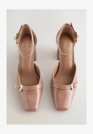 Nude Lackleder High Heels mit quadratischer Spitze, Knöchelriemen und goldener Schnallenakzent. Glatte Textur, Blockabsatzdesign, minimale Details.