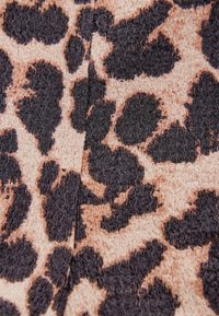 Tkanina s leopard uzorkom koja ima svijetlu bež pozadinu s velikim, crnim, teksturiranim mrljama, što pruža reljefni detalj uzorka.