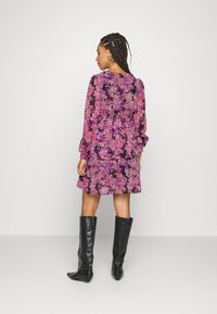 Vestido floral em roxo com um design em camadas, mangas longas e um cós elástico. Combinado com botas altas de couro pretas.