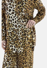 Conjunto de dos piezas con estampado de leopardo, hecho de tela ligera; cuenta con botones, un bolsillo y un ajuste relajado con patrones variados en marrón y negro.