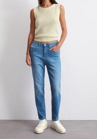 Jasnożółta dzianinowa koszulka bez rękawów, niebieskie dżinsy i białe trampki. Koszulka ma ribbową teksturę, a dżinsy są dopasowane i mają kieszenie.