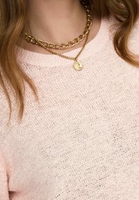 Švarkas iš šviesiai rožinės spalvos megztinio audinio su laisvu tekstūru, derinamas su sluoksniuotomis auksinėmis grandinėmis, turinčiomis apvalų pakabuką.