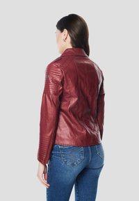 Bordová kožená bunda s rebrovanými detailmi na ramenách a rukávoch, s priliehavým strihom a spätne prešívanými gombíkmi, nosená cez modré rifle.