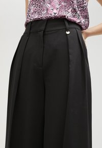 Zwarte geplooide broek met een hoge taille, een soepele stof en een zijzak, aangevuld met een klein zilveren sluitingdetail.