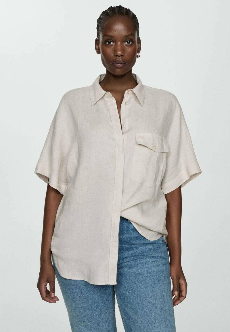 Beige short-sleeve button-up shirt made of light fabric, featuring a single chest pocket and a relaxed fit, paired with denim jeans.