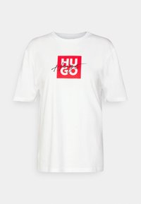 Camiseta de algodón blanca con manga corta. Presenta un gráfico cuadrado rojo con el texto negro "HUGO" y la palabra "Hugs" en cursiva superpuesta. Corte clásico.
