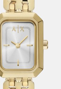 Zlata pravokotna ura s srebrnim številčnicom, ki ima minimalistične zlate kazalce, teksturirano površino in povezano zapestnico.