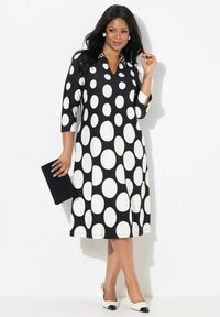 Svart och vit prickig klänning med V-ringning och trekvartslånga ärmar, med en kontrasterande krage och flödande design, som kompletteras med en svart clutchtv. 