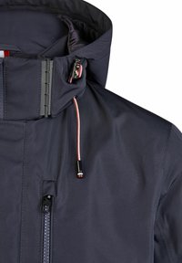 Veste bleu marine avec un col montant, une poche zippée et un cordon de serrage contrasté avec des accents en métal. Tissu texturé avec un traitement déperlant.