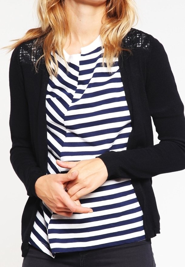 Cardigan noir avec des accents en dentelle sur les épaules, porté par-dessus un t-shirt à rayures blanches et bleu marine. Les deux vêtements présentent une coupe décontractée.