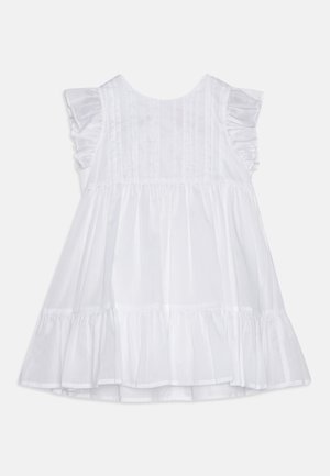 White cotton dress featuring a flared design, ruffled sleeves, and vertical stitch detailing on the bodice. Flounces at the hem.