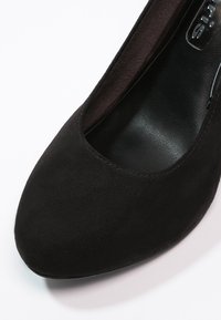 Černá semišová vysoká bota na podpatku s zaoblenou špičkou a hladkým interiérem, elegantní silueta a minimalistic design.