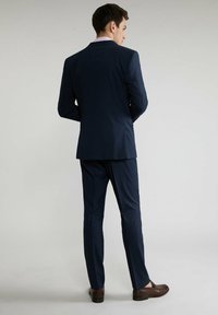 Granatowy, w kratkę, garnitur w slim fit, z jednozapięciową marynarką i dopasowanymi spodniami. Brązowe skórzane buty dopełniają całość.