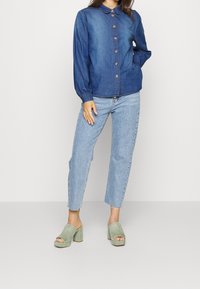 Jeansskjorta i mörkblått med krage, matchad med ljusblåa högmidjade jeans och gröna klackskor med blockklack.