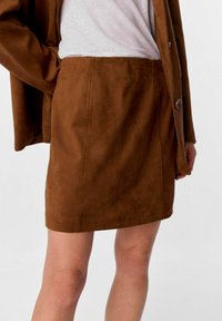 Mini gonna in suede marrone con una finitura testurizzata, dettagli sulle cuciture laterali e una linea dritta. Abbinata a una maglietta bianca morbida e a un blazer coordinato.