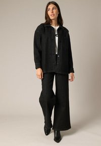 Zwarte denim overhemdjasje met knopen en een borstzak, gecombineerd met brede zwarte denim broek en zwarte puntige enkellaarsjes.