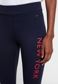 Leggings bleu marine en tissu extensible, ornés d'un imprimé rouge vif "NEW YORK" sur le côté et d'un petit logo près de la taille.