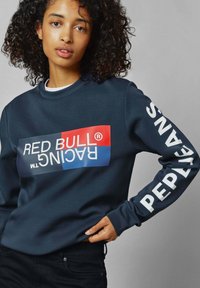 Sudadera de color marino con un gran gráfico multicolor que lleva "RED BULL® RACING" en blanco y el texto "PEOPLE" en la manga. Textura suave.