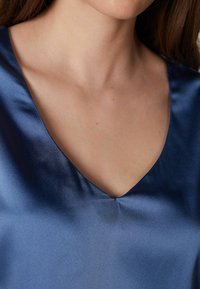 Top de satén azul marino con escote en V. Textura suave con un ligero brillo, que enfatiza la simplicidad en el diseño y el color.