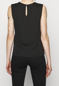 Černý bezrukávový top s detaily ve tvaru klíčové dírky na zádech, hladkým povrchem a rovný střih, spárovaný s tmavými džíny.