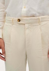 Beige maßgeschneiderte Hosen aus glattem Leinen mit Vorderfalten und einem Knopfverschluss am Bund.
