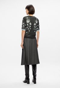 Μαύρο, λαμπερό πλεκτό πουλόβερ με λουλούδια κεντημένα, κοντά μανίκια και ανοιχτό μπλε λεπτομέρειες, σε συνδυασμό με μια πλισέ γκρι φούστα και μαύρες μπότες μέχρι το γόνατο.