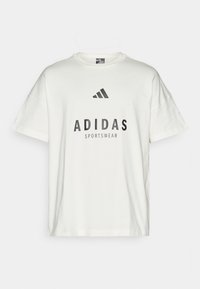 Biela bavlnená tričko s krátkymi rukávmi, okrúhlym výstrihom a výraznou čiernou typografiou s nápisom "ADIDAS SPORTSWEAR" s logom nad ním.