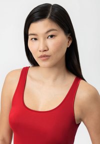 Top rosso senza maniche con scollo a barca, realizzato in un materiale liscio e elasticizzato. Presenta spalline sottili e una vestibilità aderente.