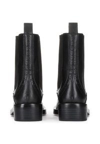 Botas de tobillo de cuero negro con punta redonda, costuras laterales texturizadas y un tacón bajo apilado. Incluyen tiradores traseros para facilitar el uso.