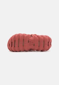 Red molded foam shoe with a wavy design, featuring cutouts and a textured surface for breathability and flexibility.