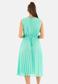 Un vestido sin mangas de color verde menta, plisado, con una cintura ajustada, que presenta una textura suave y una falda fluida que cae por debajo de la rodilla.